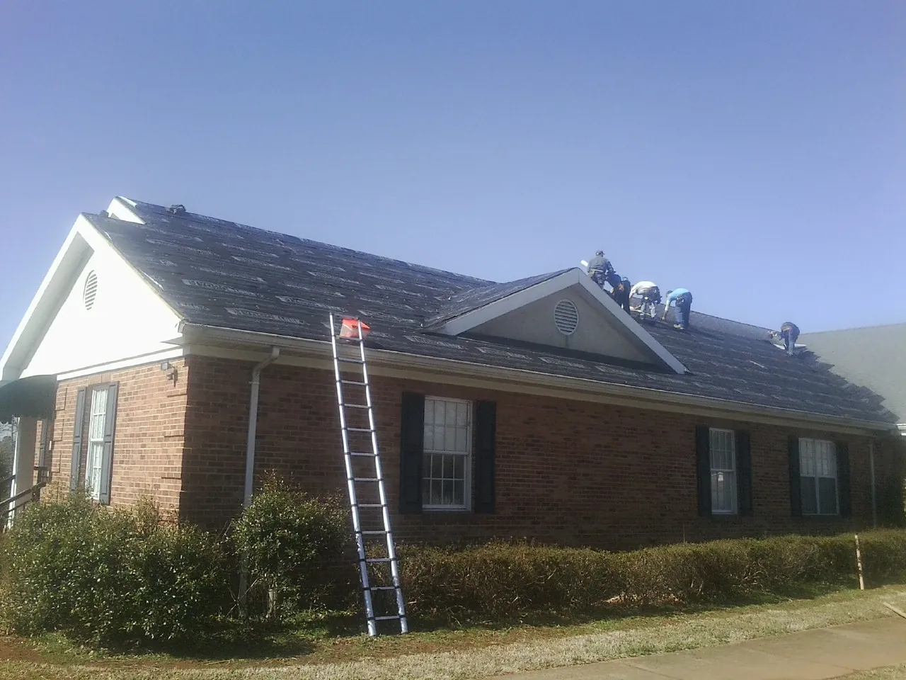 Crew tearing shingles off a brick ranch roof with a ladder set — Emergency Roof Repair work by our crew in Rufe