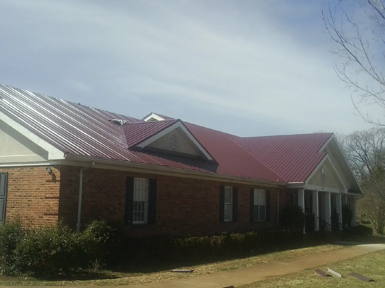 Red metal roof with gabled entries on a long brick building, from a Hail Damage Roof Repair job in Rufe