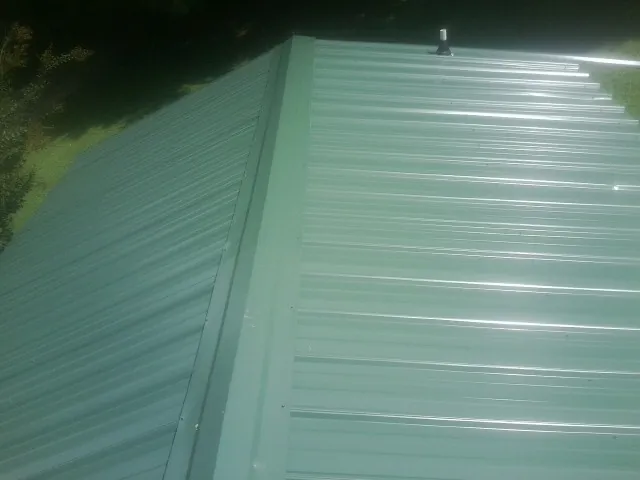 New green metal panels meeting at the ridge of a roof — Flat Roof Repair work by our crew in Rufe