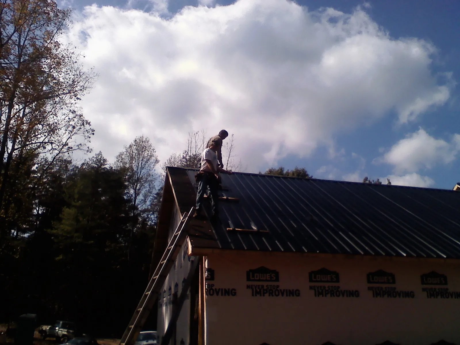 Roofer fastening dark metal panels high against a cloudy sky, from a Roof Inspection job in Rufe