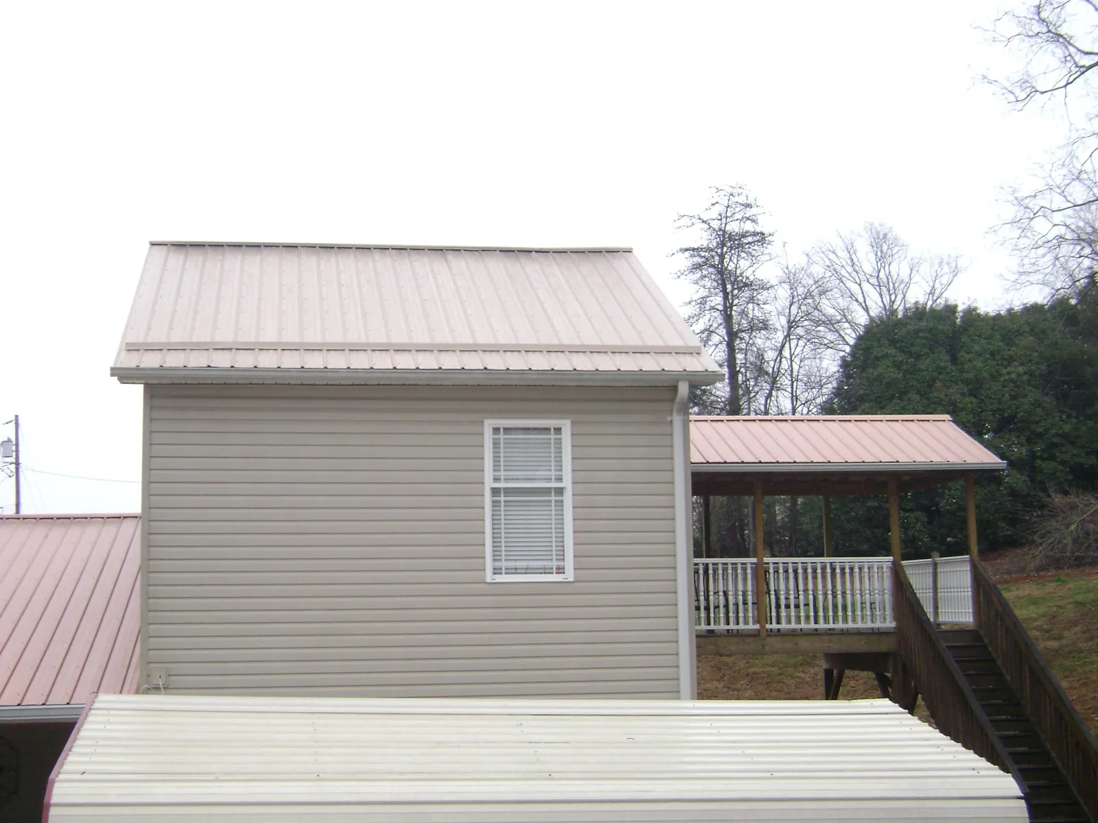 Tan metal roofs on a two story addition and attached porch, from a Roof Replacement job in Rufe